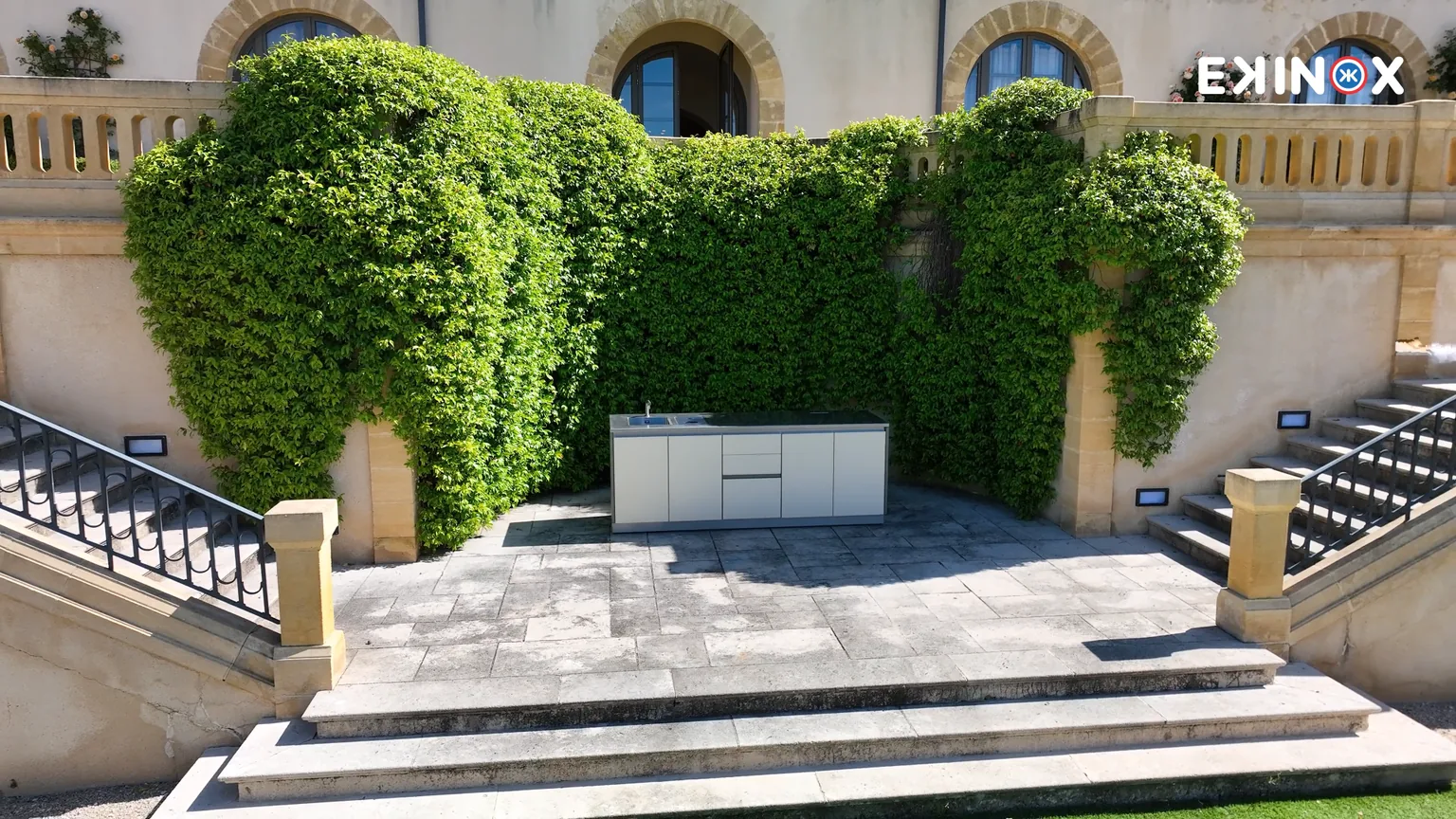 La cuisine d'extérieur mobile ROLYX posée seule au milieu d'une terrasse dallée, entre deux escaliers de pierre, sans aucun raccordement apparent
