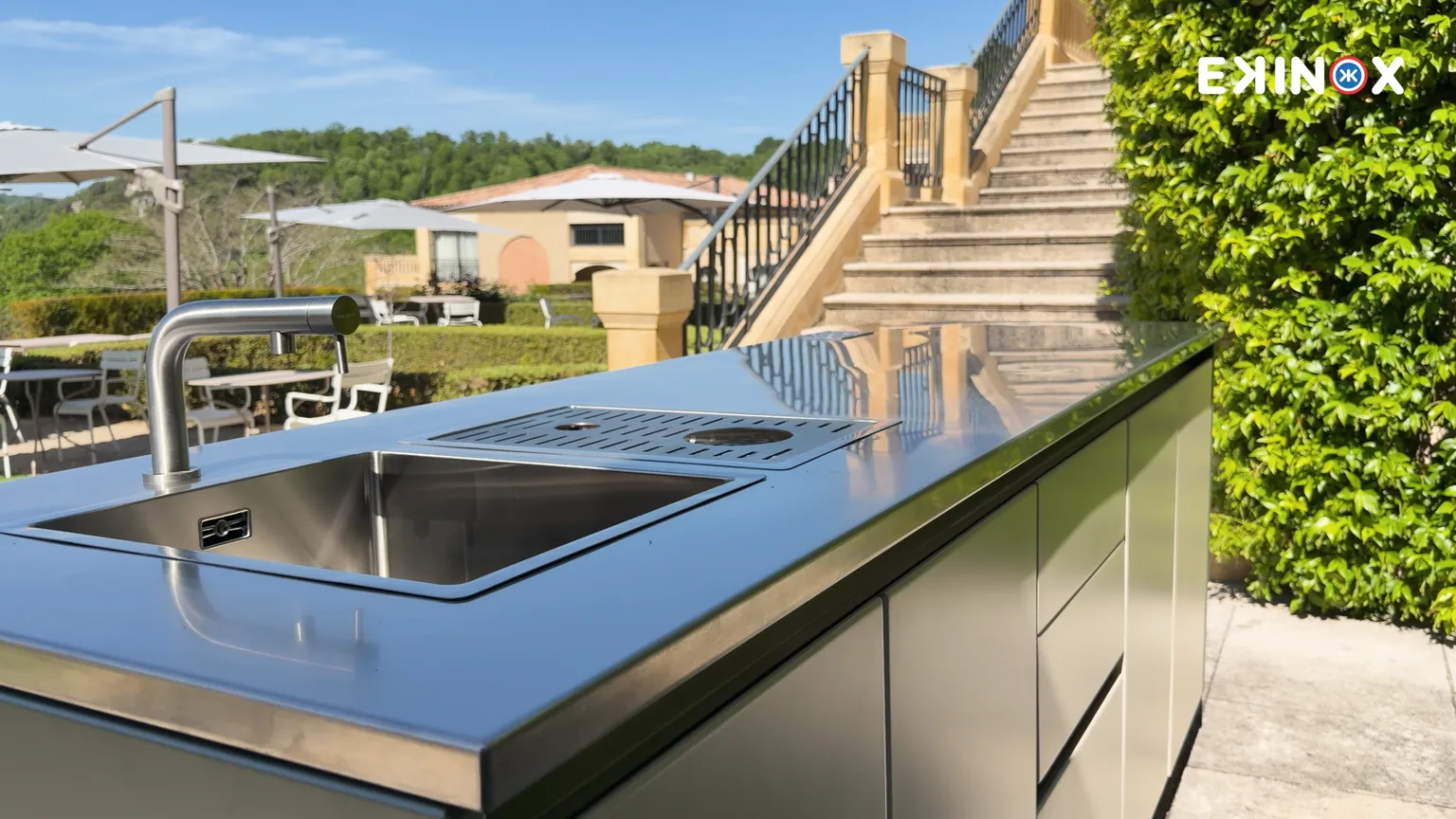 Plan de travail en inox de la cuisine d'extérieur ROLYX, évier encastré et rince-verres, sur une terrasse ensoleillée