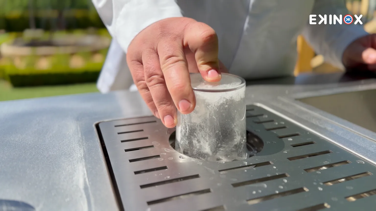 Rince-verres encastré dans le plan de travail en inox d'une cuisine d'extérieur ROLYX, verre en cours de rinçage