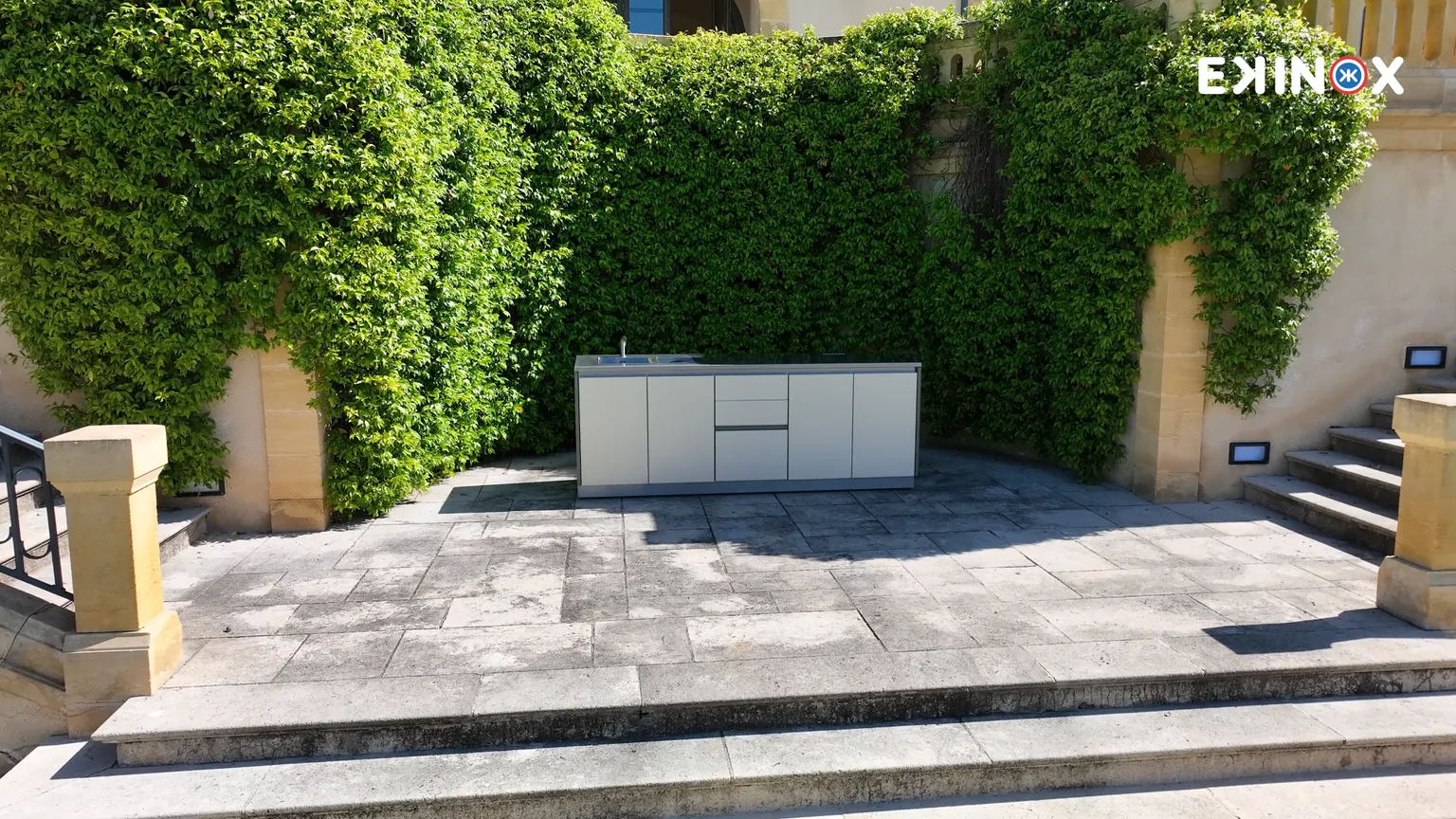 La cuisine d'extérieur mobile ROLYX installée sur une terrasse en pierre, devant un mur de verdure, au Domaine de Rochebois