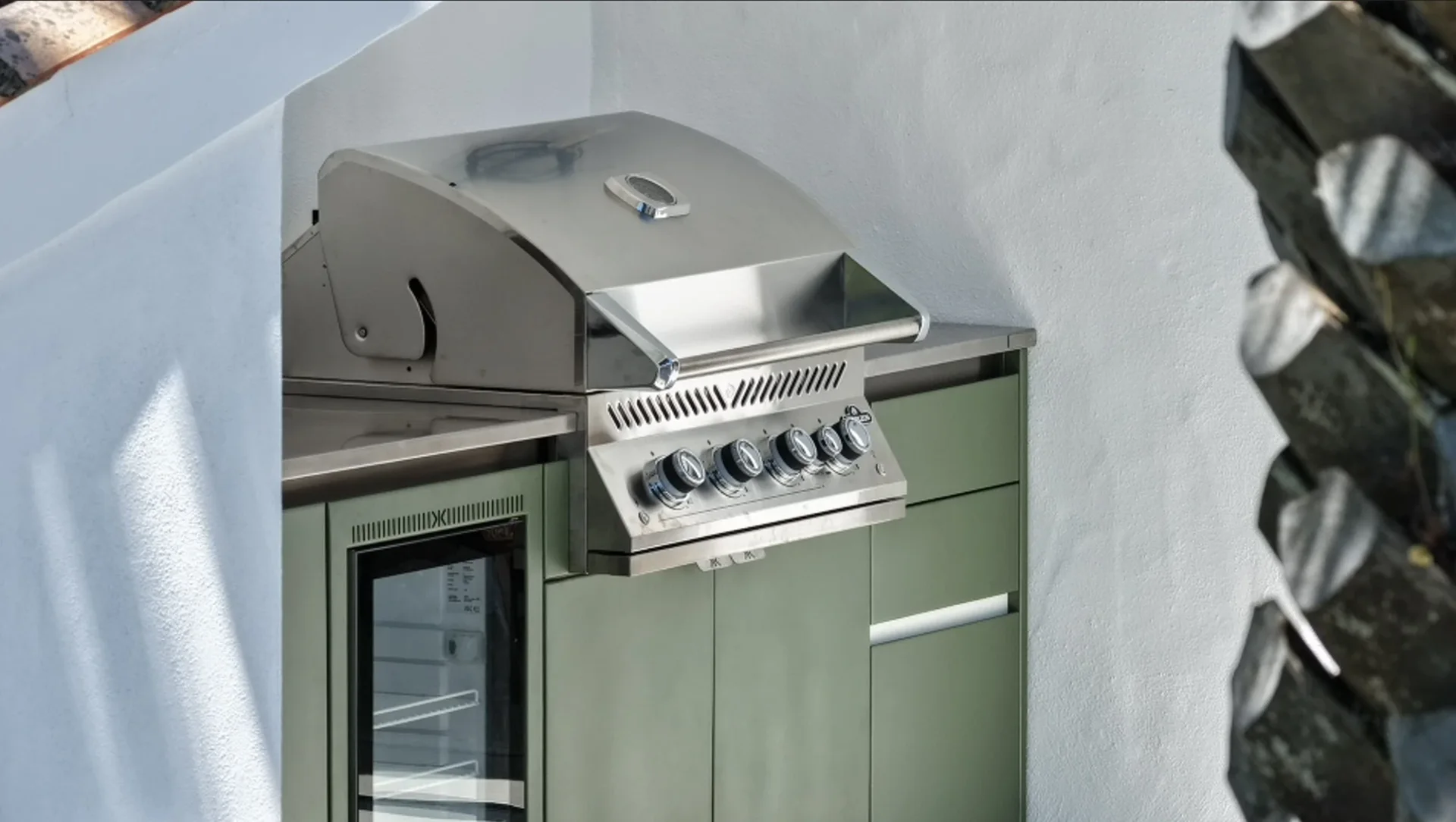 Le barbecue à gaz et le réfrigérateur encastrés dans la cuisine EKZALT aux façades vertes, contre le mur