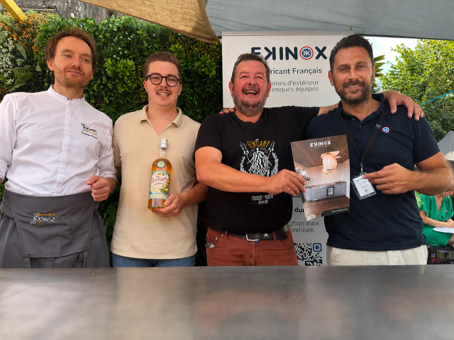 Le chef Thomas Perron et des partenaires de la fête devant le stand EKINOX, avec une bouteille de liqueur de gentiane