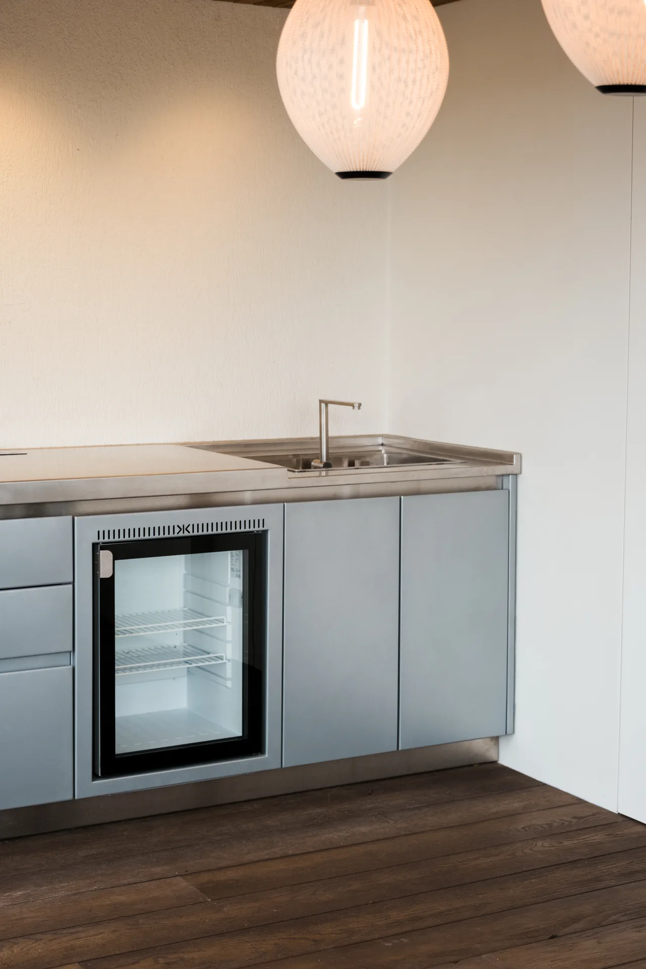 Le réfrigérateur encastré derrière sa porte vitrée et l'évier en inox de la cuisine SOLSTYS, de près