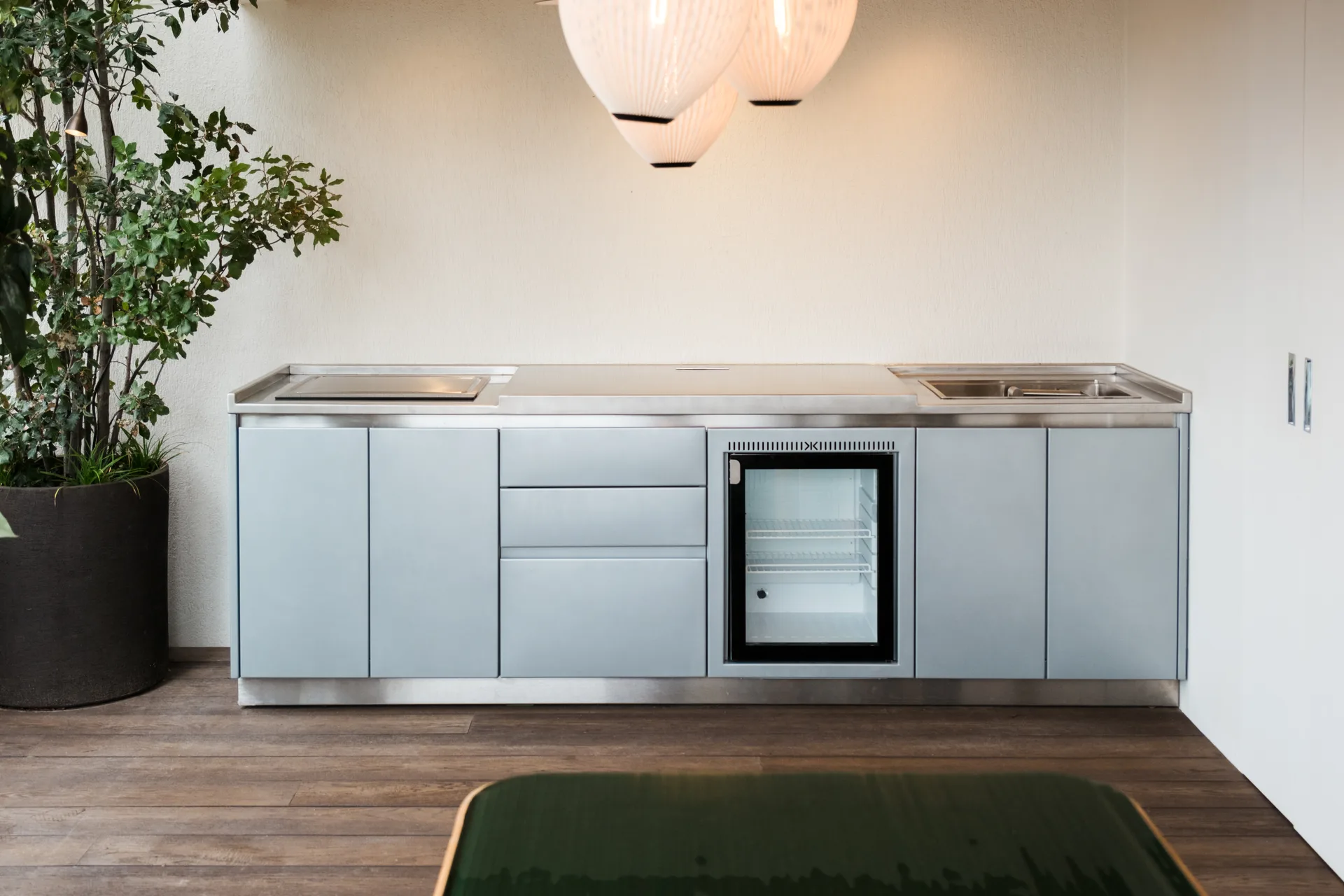 La cuisine SOLSTYS sous trois suspensions en papier plissé, la table verte au premier plan