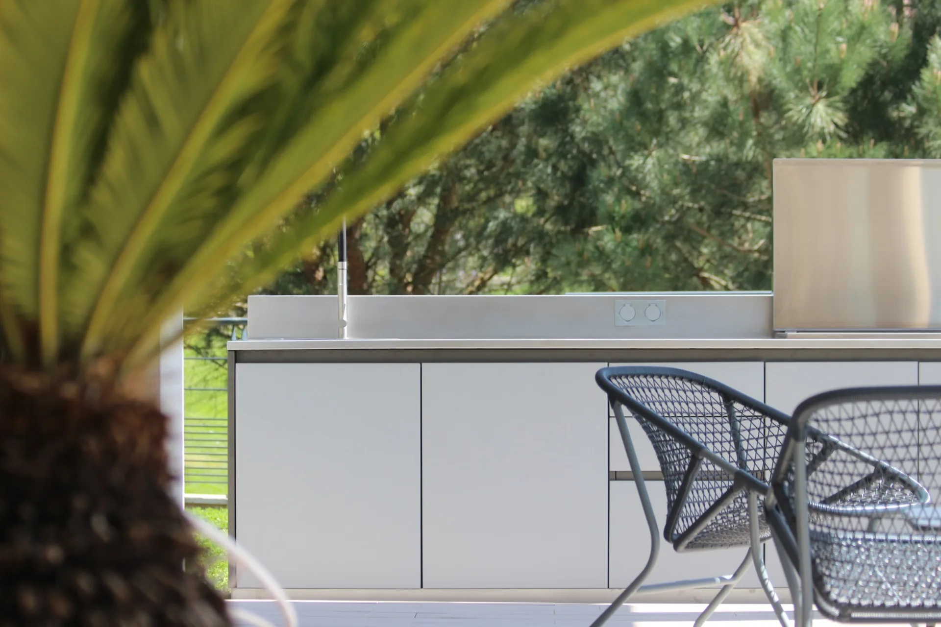 La cuisine X-PRESS sur sa terrasse, derrière une palme et deux fauteuils de jardin